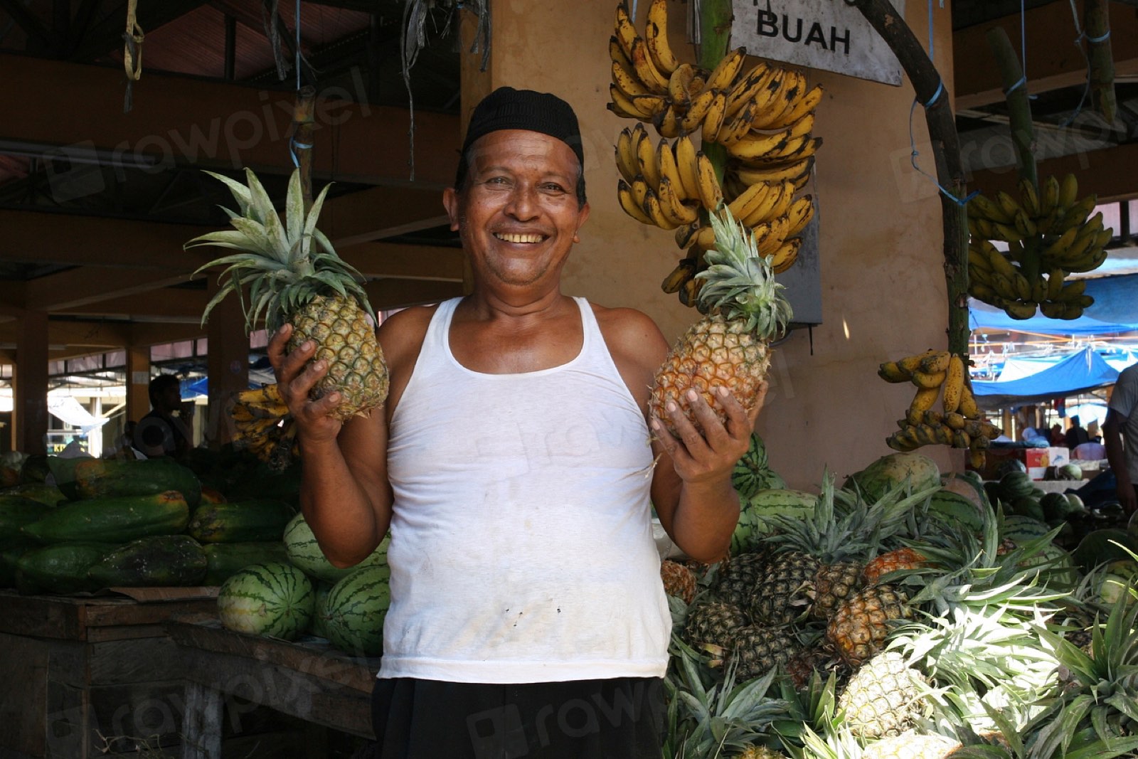 A smiling fruit seller holding pineapples